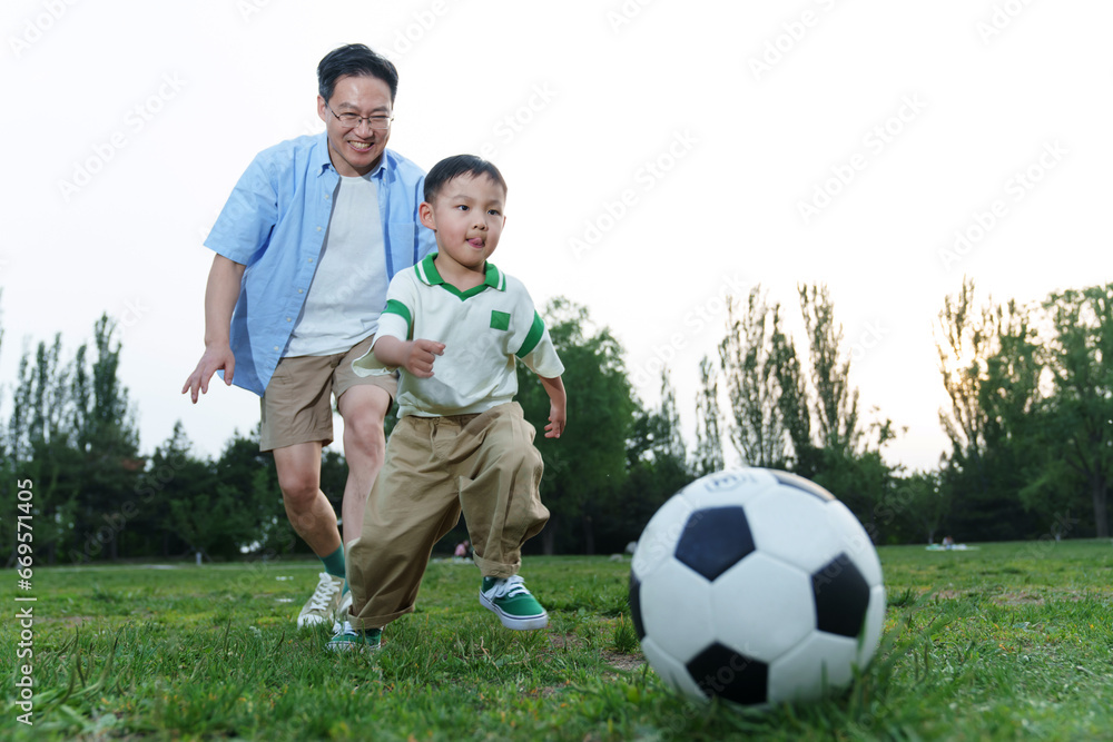 Happy father and son are playing football on the grass Happy father and son are playing football on the grass
