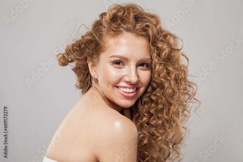 Beautiful joyful model woman with wavy hairstyle having fun on gray background. Pretty young woman with curly hair, clear skin, natural makeup and cute smile