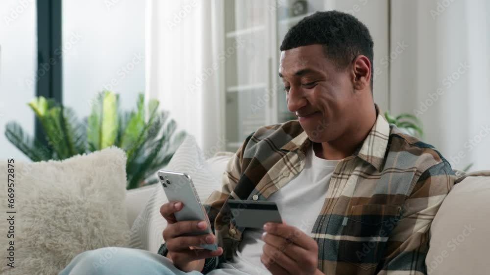Happy African American man at home couch sofa guy user buyer male client banking buying shopping online with credit bank card and mobile phone smartphone e-commerce order delivery payment internet pay Happy African American man at home couch sofa guy user buyer male client banking buying shopping online with credit bank card and mobile phone smartphone e-commerce order delivery payment internet pay