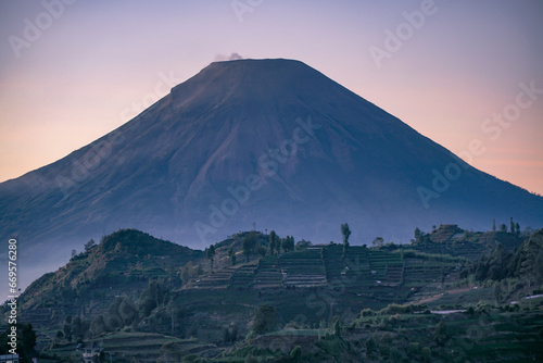 Telephoto of peak of Sindoro Mountain with hills in sunrise time. Dieng Regency, Indonesia