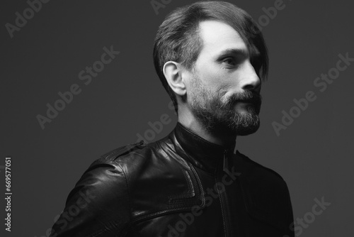 Rock star concept. Profile portrait of fashionable handsome mature biker in leather jacket over dark gray background. Close up. Copy-space. Retro style. Black and white studio shot