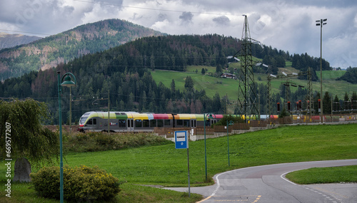 Ein Zug der italienischen Eisenbahn, fährt durch eine grüne Landschaft, mit Wiesen und Wäldern am Berg im Hintergrund