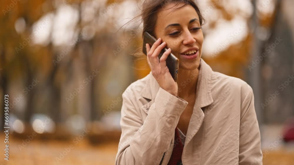 Woman with phone in autumn park. Young elegant woman in colorful golden autumn park use cell phone audio voice message recognition. smiling girl is talking on a smart phone Woman with phone in autumn park. Young elegant woman in colorful golden autumn park use cell phone audio voice message recognition. smiling girl is talking on a smart phone