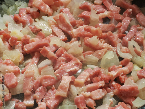 Close view of a sauté of lardons and onions in a pan, while they are cooked