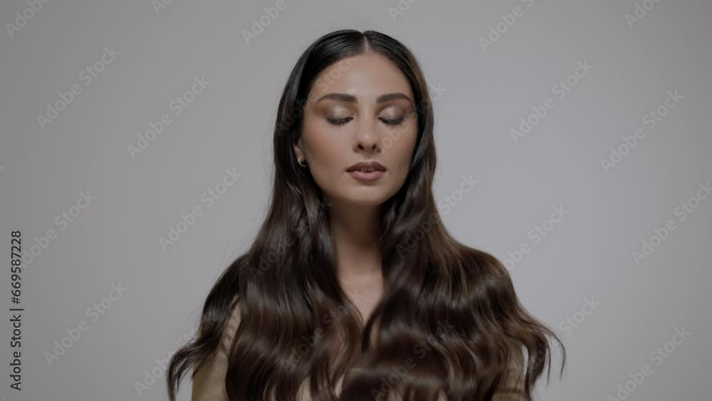 Young charming brunette woman with long wavy hair posing on a light gray background. Young charming brunette woman with long wavy hair posing on a light gray background.