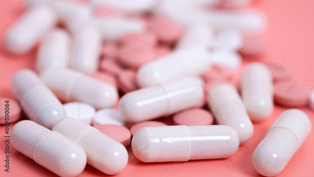 Many pink and white pills in capsules. Medical treatment with medicine, vitamins or nutrition supplements. Woman health. Textured background. Close up, selective focus