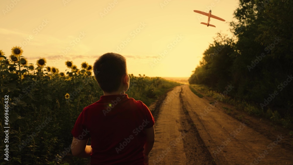 Boy launches plane into field with sunflowers at sunset. Little boy playing with toy airplane against background summer nature in outdoor field. Concept kids dream flight. Kids game with an airplane