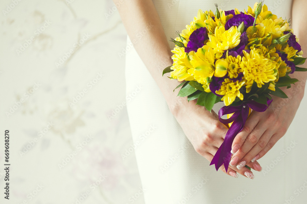 Hands of bride with wedding bouquet made of violet and yellow flowers over stylish white dress. Vintage background. Retro style. Close up. Copy-space. Indoor shot