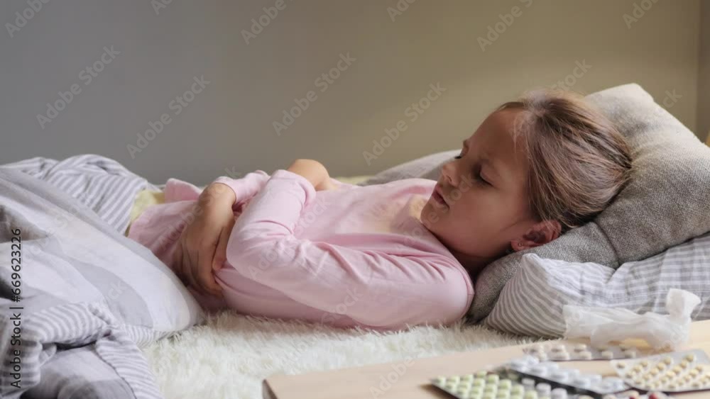 Medical illness. Child's health. Unhealthy girl feeling severe pain in her stomach holding her stomach while lying on the bed grimacing from strong pain needs doctor help. Medical illness. Child's health. Unhealthy girl feeling severe pain in her stomach holding her stomach while lying on the bed grimacing from strong pain needs doctor help.