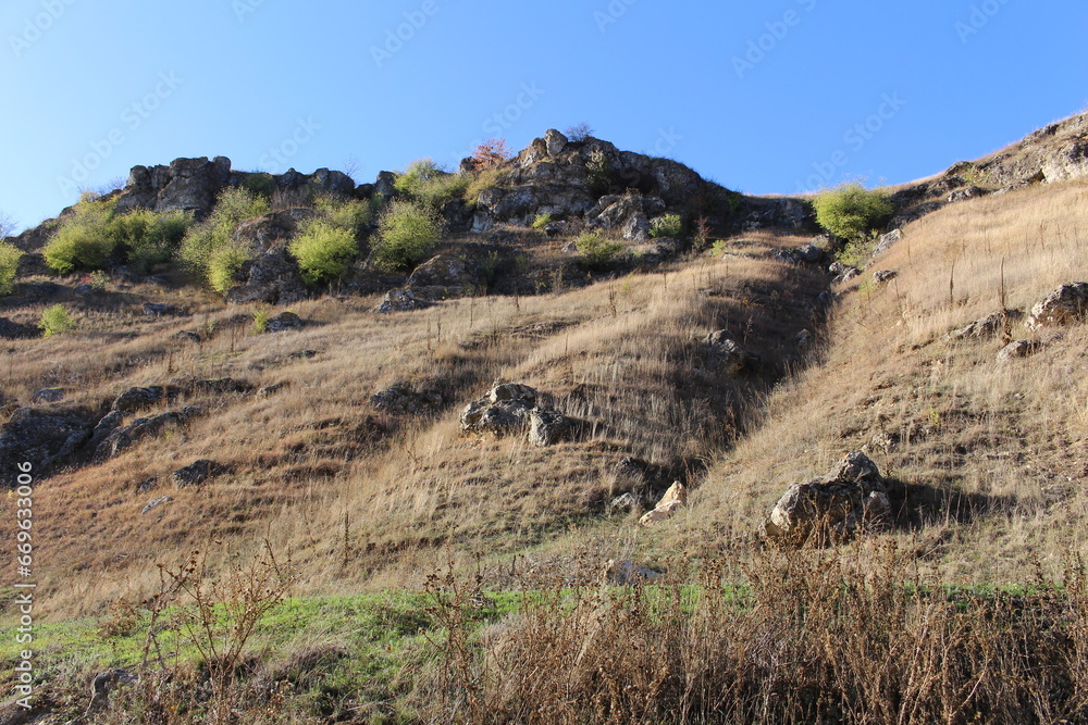 A rocky hillside with a grassy hill and a blue sky