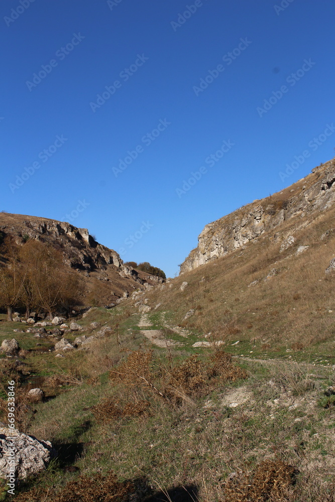 A grassy hill with a rock wall and a blue sky