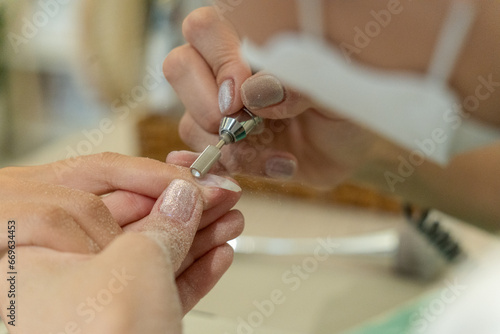 close up of beautician with electric nail drill in beauty manicure salon. Nail manicure treatment with electric machine