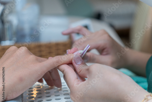 Nails manicure detail with file or brush item. Woman beautiful nail care process. Closeup of female hands filing nails with professional nail file in beauty nail salon.