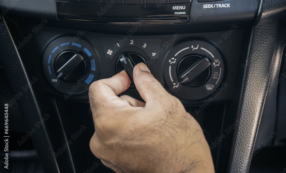 Close-up of a male driver's hand turning on the air conditioning in the car.The hand is holding the switch to turn on the air conditioning inside the car.
