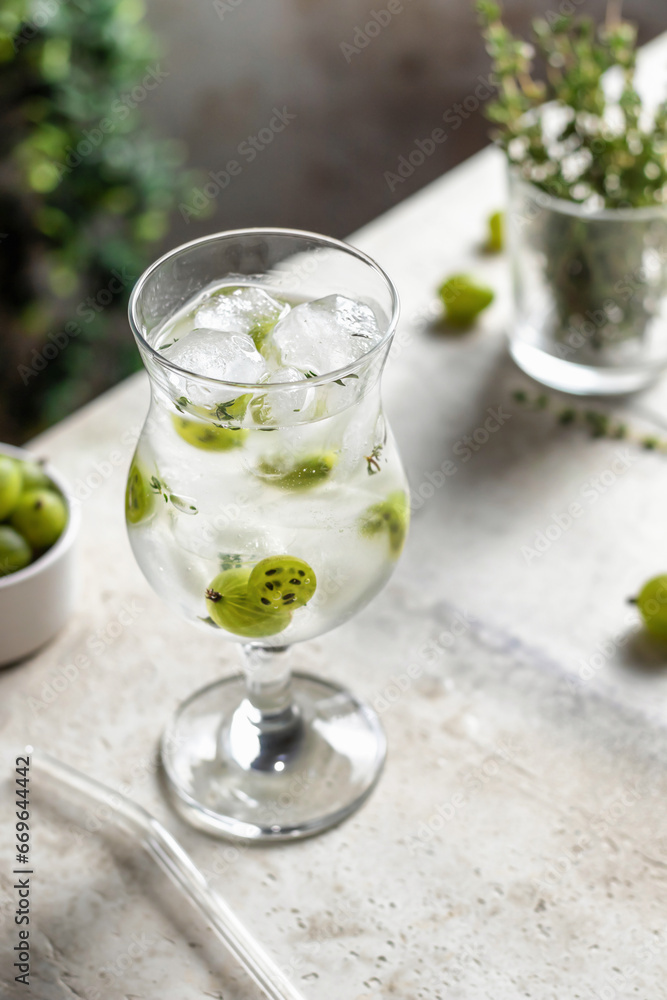 Fototapeta premium Glass of refreshing iced detox drink with gooseberries and thyme. Infused water or berry cocktail