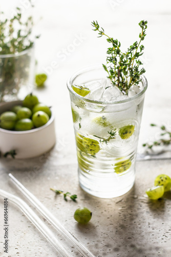 Glass of refreshing iced detox drink with gooseberries and thyme. Infused water or berry cocktail