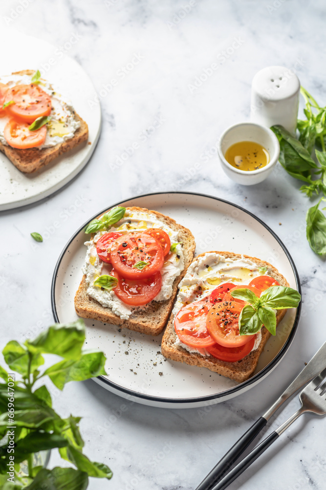 Sandwiches or toasts with tomatoes, cream cheese, olive oil and basil on a plate on white marble background. Traditional italian mediterranean food Sandwiches or toasts with tomatoes, cream cheese, olive oil and basil on a plate on white marble background. Traditional italian mediterranean food