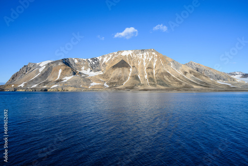 Peaceful sunny blue landscape of arctic ocean, rocky mountain range with snow, and blue sky, Gashamna, Svalbard 