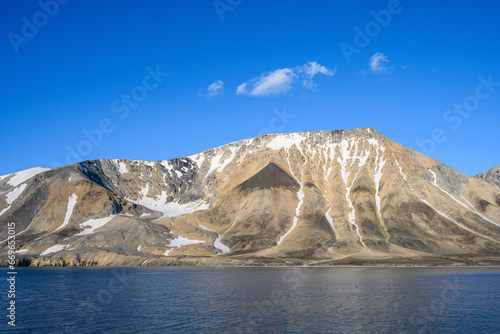 Peaceful sunny blue landscape of arctic ocean, rocky mountain range with snow, and blue sky, Gashamna, Svalbard 