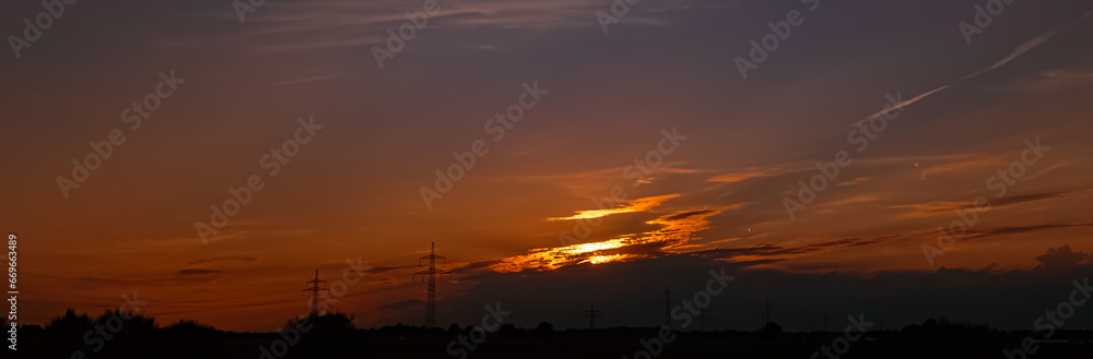 Sunset with a dramatic sky and overland high voltage lines near Tabertshausen, Deggendorf, Bavaria, Germany