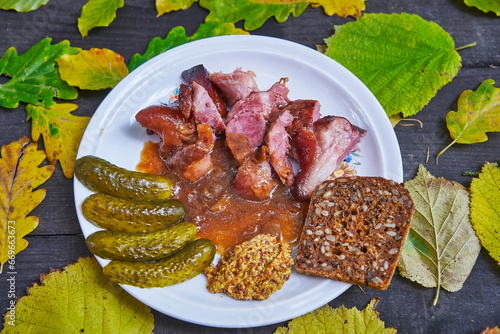 Typical autumn seasonal delicacy from cuisine of Czech republic. Unboned smoked pork knuckle slowly roasted in dark beer and onions and served with rustic mustard, pickles and slice of rye seed bread