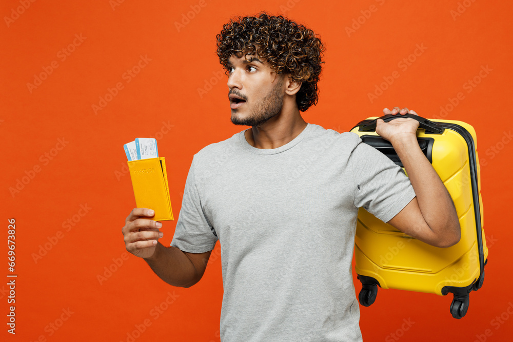 Traveler sad Indian man wear t-shirt casual clothes hold suitcase passport ticket isolated on plain orange background. Tourist travel abroad in free time rest getaway. Air flight trip journey concept. Traveler sad Indian man wear t-shirt casual clothes hold suitcase passport ticket isolated on plain orange background. Tourist travel abroad in free time rest getaway. Air flight trip journey concept.