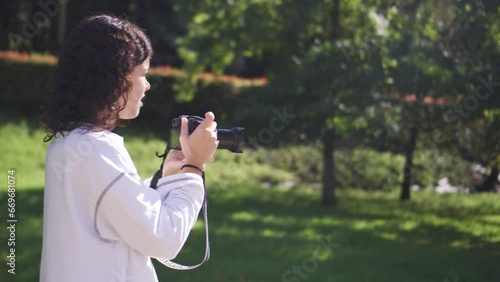 Young brunette girl in white sweatshirt with telephoto camera photographing wildlife in natural environment
