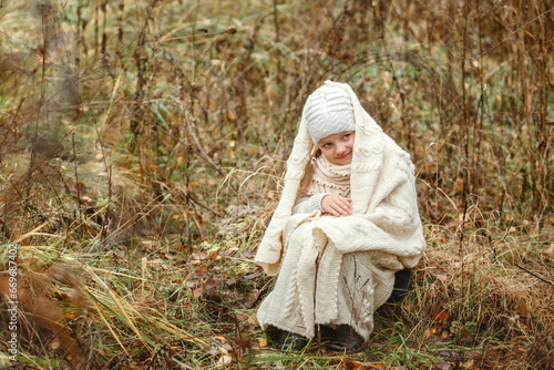 Portrait of a smiling young girl sitting in a park wrapped in a white blanket.