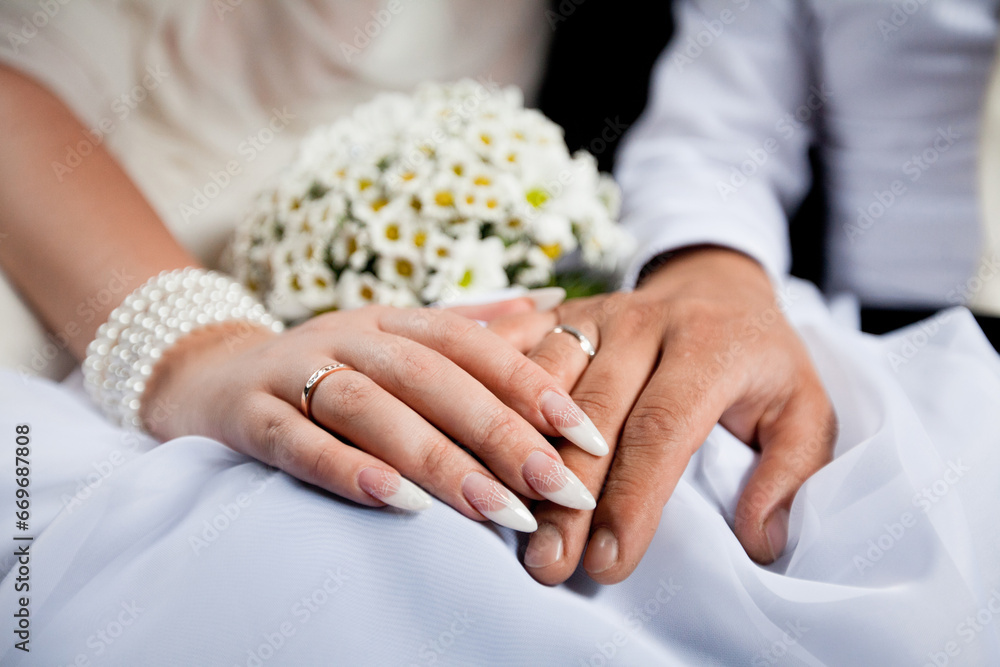 Bride and Groom's Interlocked Hands with Wedding Rings, Next to a Bouquet of White Flowers Bride and Groom's Interlocked Hands with Wedding Rings, Next to a Bouquet of White Flowers