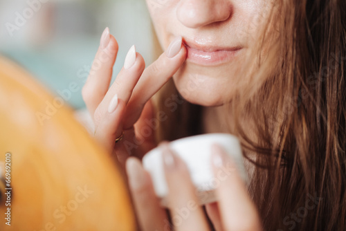 Woman using vaseline on her mouth. Closeup lips background. Applying vaseline on lips with finger. Beauty background. Young girl skin care. Cosmetics for moisturize. Table mirror face reflection. photo