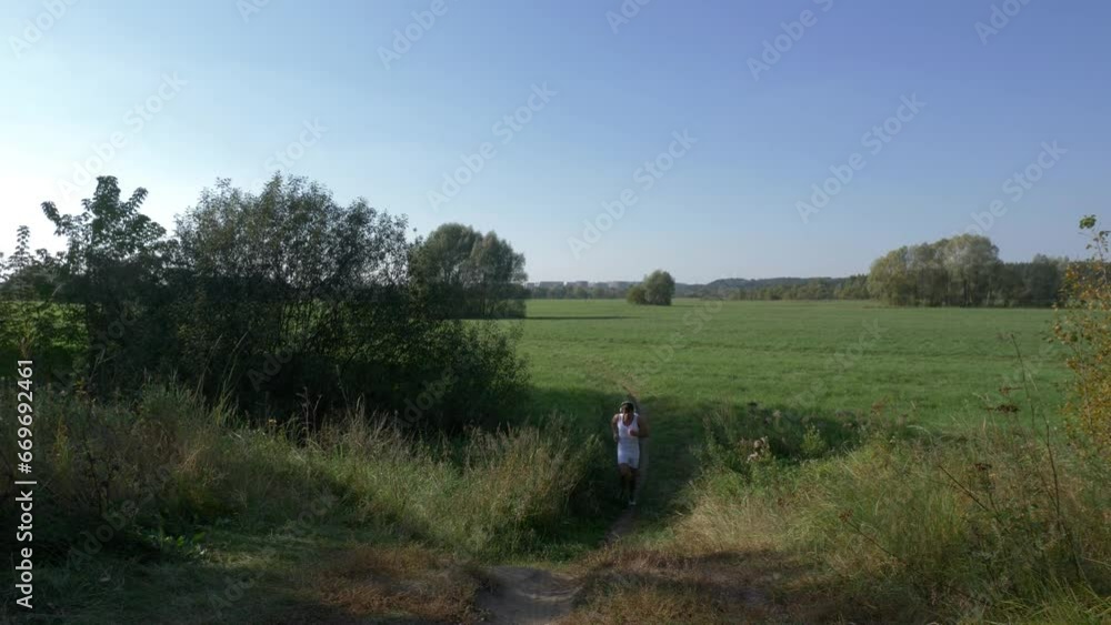 Sweaty runner in white overalls and headphones on his head jogging on a green meadow Sweaty runner in white overalls and headphones on his head jogging on a green meadow