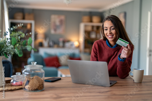 Beautiful smiling businesswoman doing online shopping over laptop with credit card at desk in home office.