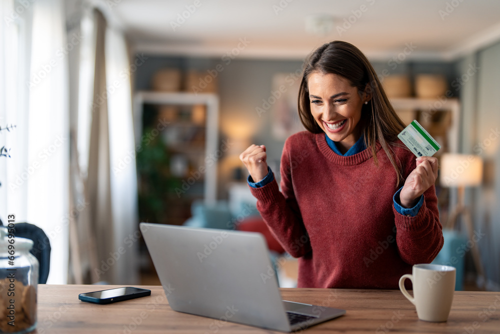 Enthusiastic charming millennial woman feeling excited looking at laptop screen holding credit card, raising fist in yes gesture satisfied with online payment possibilities, rejoicing approved loan. - obrazy, fototapety, plakaty 