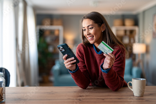 Happy young woman using smart phone shopping online with a credit card.