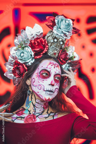 Fototapeta Naklejka Na Ścianę i Meble -  Mexican woman dressed and characterized as a catrina for the Day of the Dead festivity, behind her an orange background like the cempasuchil flower.