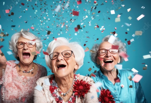 three happy senior women at new year party with confetti dancing on blue background, celebrating holiday season or birthday