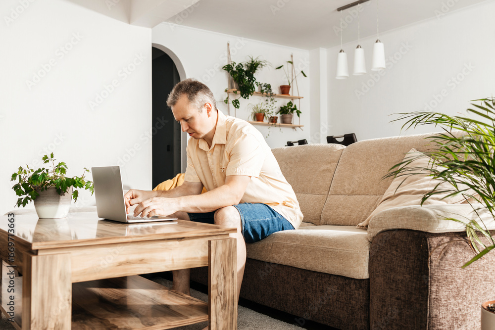 Successful happy freelancer working on laptop at home. A man sits on the sofa and uses a laptop to shop and communicate online Successful happy freelancer working on laptop at home. A man sits on the sofa and uses a laptop to shop and communicate online