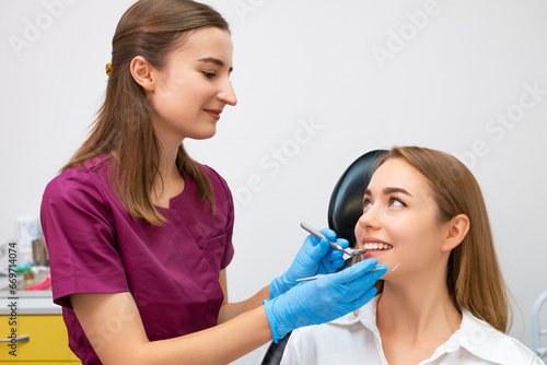 Cheerful female dentist holding dentist tool near smiling young patient.