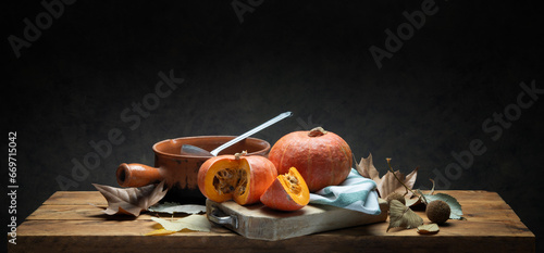Pumpkins on rustic wooden table with old terracotta pan, dry leaves and dark gray background, space for text.