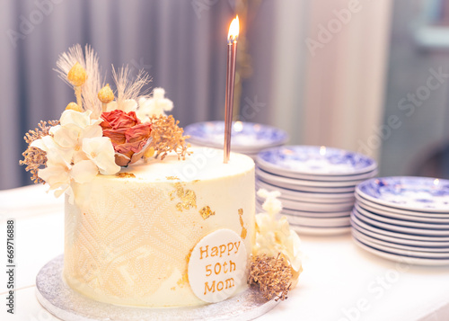 Mom's 50th birthday cake with lighted candle and plates background blur selective focus noise