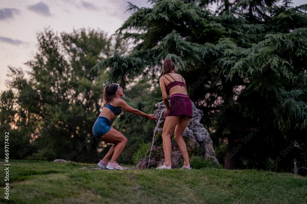 Fit and muscular women having fun outdoors, splashing water, and enjoying a lively evening in a park. Fit and muscular women having fun outdoors, splashing water, and enjoying a lively evening in a park.