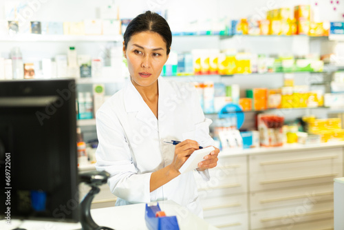 Medicine, profession and healthcare concept - female doctor or pharmacist in white coat with notebook and pen writing medical report over pharmacy background Free Download Medicine, profession and healthcare concept - female doctor or pharmacist in white coat with notebook and pen writing medical report over pharmacy background - GFXLoad