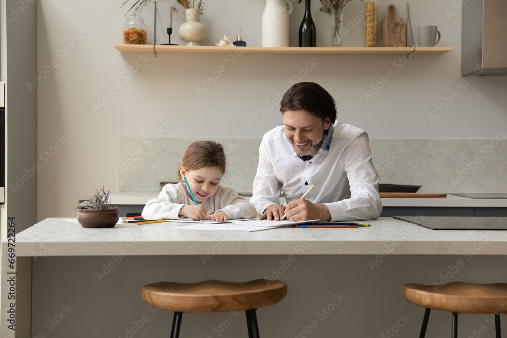 Happy cheerful father teaching to draw adorable little daughter girl. Dad and sweet kid enjoying home learning creative activity, making doodles in paper albums with colored pencils. Fatherhood