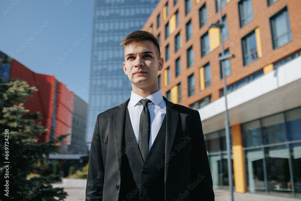 With city buildings as his backdrop, a professional young Caucasian American businessman in a business suit showcases determination and style.