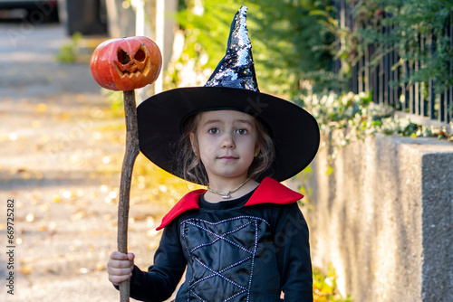 Portrait of a girl dressed as a Veolia witch with broom and hat, Halloween pumpkin set on a stick. Concept: All Saints' Day, Halloween, costume show.
