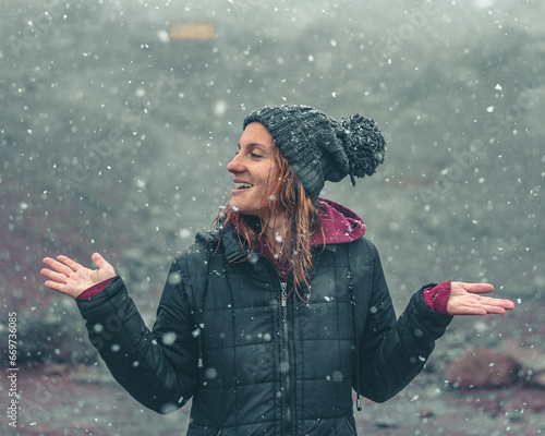 mulher com touca de lã e mãos levantadas, sorrindo, em cenário de inverno com neve caindo  photo