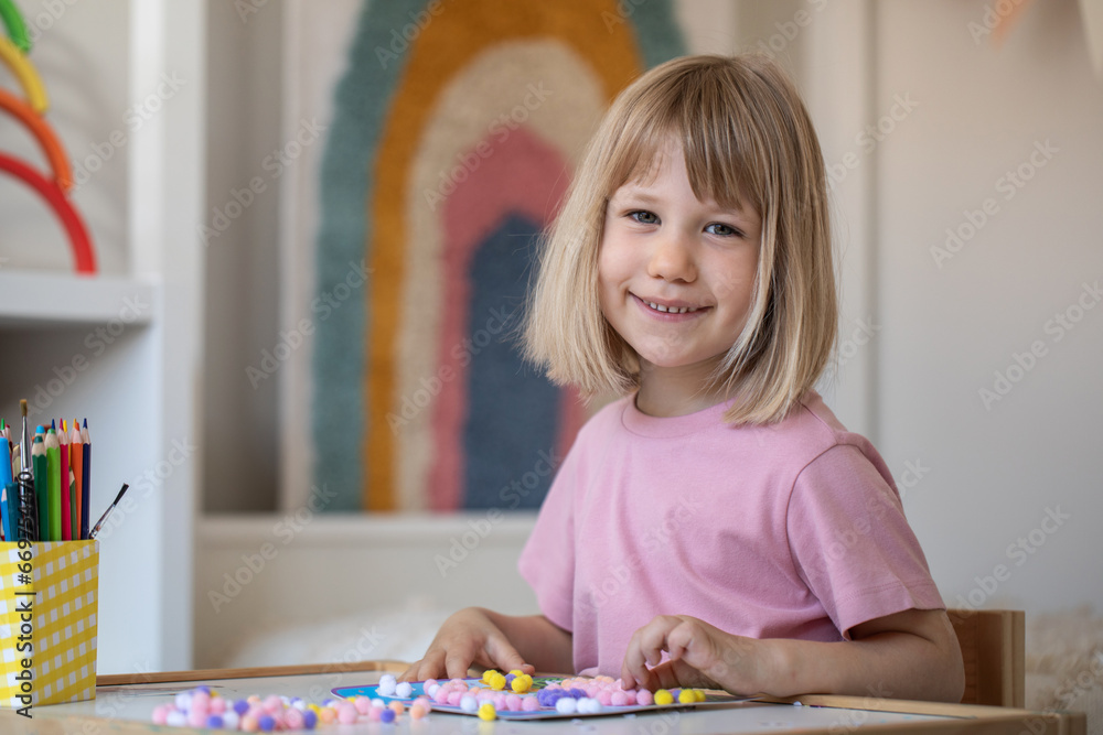 Fototapeta premium A cute girl makes crafts sitting at a table in the children's room. Development and preschool education.