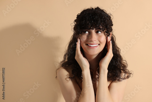 Portrait of beautiful young woman in sunlight on beige background, space for text