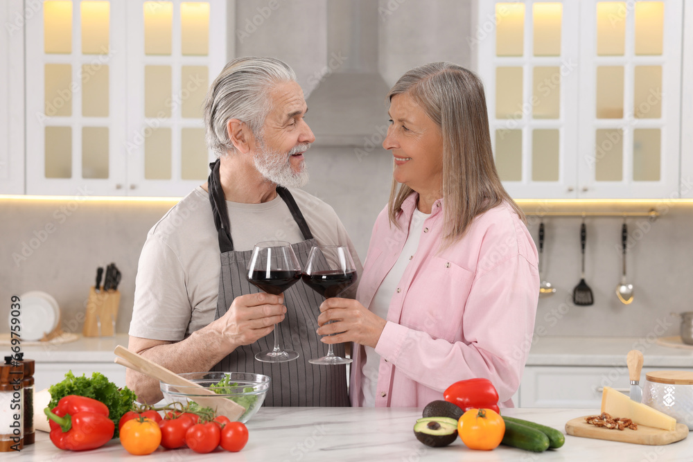 Happy affectionate senior couple with glasses of wine in kitchen Happy affectionate senior couple with glasses of wine in kitchen
