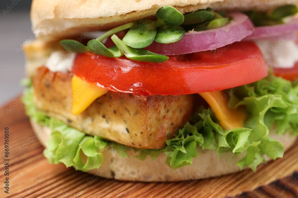Delicious burger with tofu and fresh vegetables on wooden board, closeup